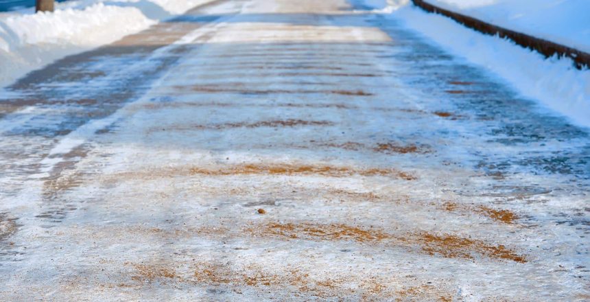 Sidewalk covered with sand and salt mixtures. Prevent slips on ice in city. Salt and sand melt ice on roads and walkways. Deicing chemicals on pavement. Prevent slipping on road with deicing reagents